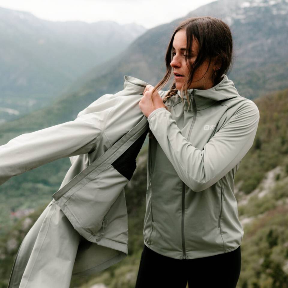 Wanderin in nebeliger Berglandschaft zieht sich eine Regenjacke an