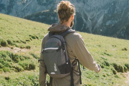 Mann mit Rucksack wandert in einem grünen, bergigen Gebiet.