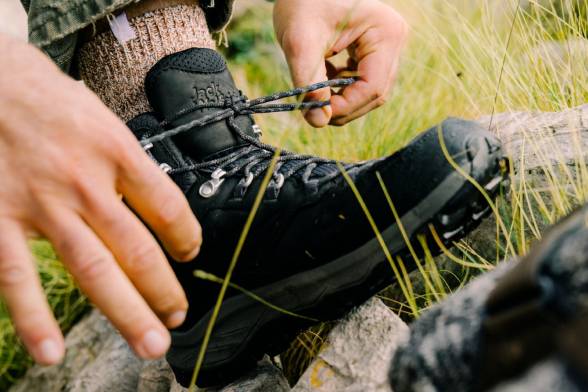 Nahaufnahme eines Mannes in schwarzen Wanderschuhen beim Schuhbinden